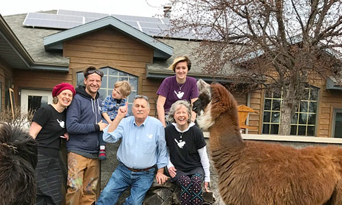 Ron and Kathy Gray, front right, along with (left to right) their daughter Miranda, son-in-law Scott, and grandchildren Murdock and Gwendolyn, pose with their rooftop solar energy system. Llamas from their family business join in the fun.