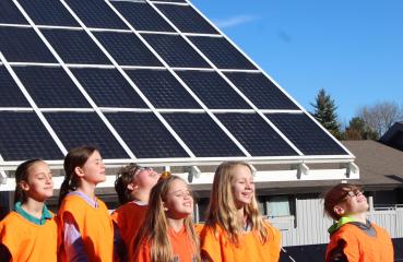 Students smiling at the sky in front of a solar panel