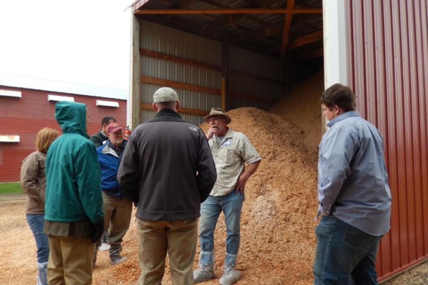 Viking Company owner Bill Koenig of Albany, MN shows tour participants the wood fuel storage bunker containing two types of fuel used in the biomass heating system for one of his broiler chicken barns.