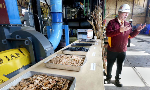 Don Fosnacht, NRRI associate director of the Renewable Energy Initiative, describes the process of converting wood (foreground) into compact briquettes that can be used in coal-fired power plants. Photo by Bob King, Duluth News Tribune