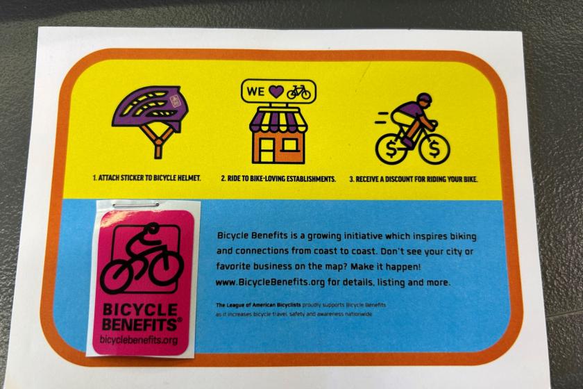 A photo of a promotional flyer showing illustrated images of a bike helmet, a building, and a bicycle. Words on flyer are indistinct. 