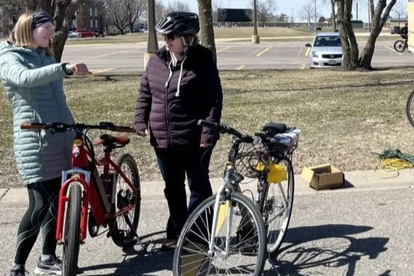 Two women in coats standing next to bicycles in a parking lot.