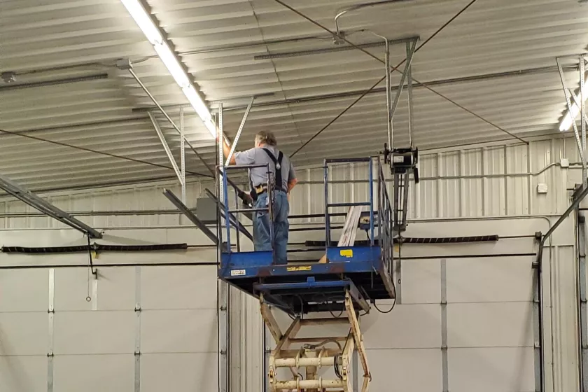  Inside of Comfrey’s fire hall, a person is standing atop a mechanical lift while installing LED lights.