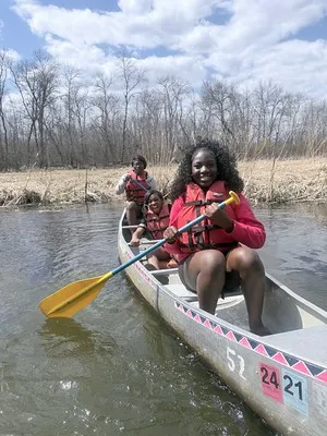 Three young Black women smiling in a canoe on the water. 2026.