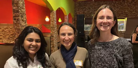  Three women stand together smiling. 