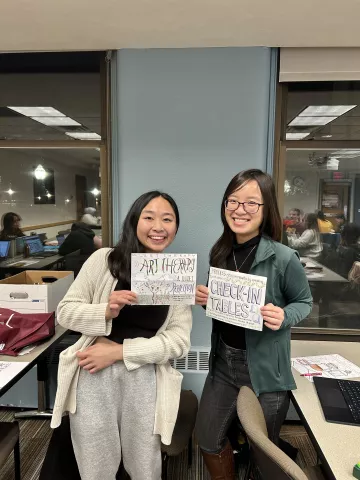 Left to right: Joyce Wong and Thi Ngyuen holding calligraphy signs 