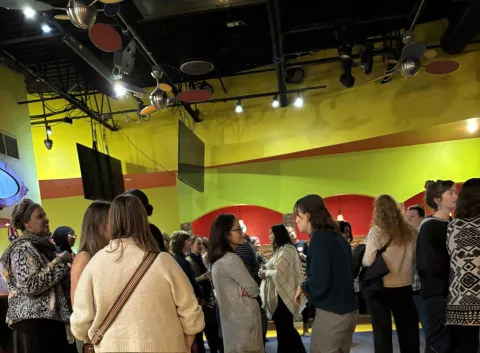 A group of women casually mingling in a bright colored restaurant setting. 