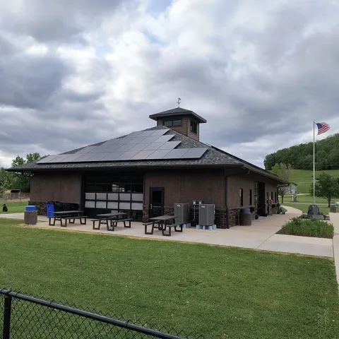 Large brown building in a park has a slanted roof with solar panels on two sides.