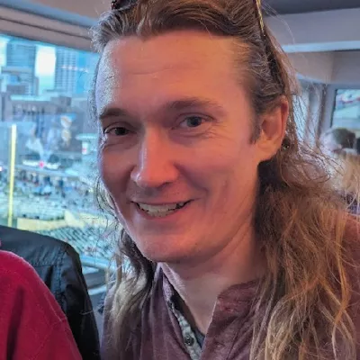 A white-presenting man with shoulder length dark blonde hair.