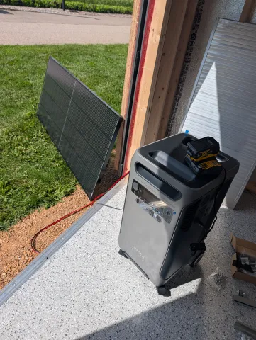  A solar panel sits outside next to a large box in the shed.