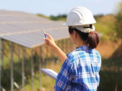 hardhat wearing person holding a clipboard and pointing a pencil at a solar array