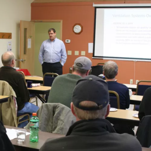 person gives presentation in front of group sitting at tables