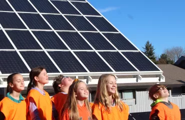 Students smiling at the sky in front of a solar panel