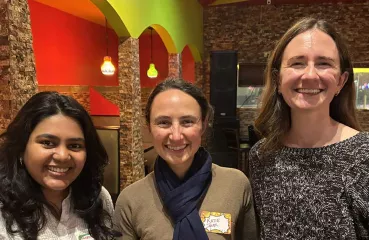  Three women stand together smiling. 