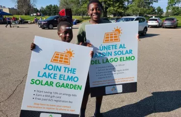 Two kids outside, smile while holding signs promoting the Lake Elmo Solar Garden.