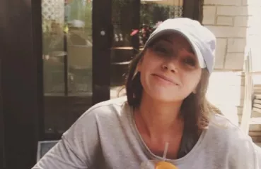 Rau looks casual as she sits outside smiling over a beverage.
