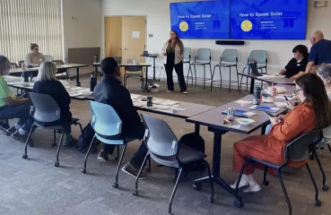 Conference room with people sitting o tables surrounding the presenter.