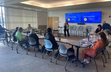 Conference room with people sitting o tables surrounding the presenter.