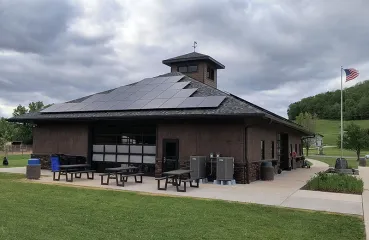 Large brown building in a park has a slanted roof with solar panels on two sides.