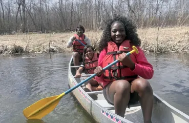 Three young Black women smiling in a canoe on the water. 