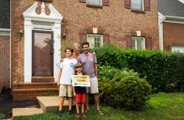 Family of three posing in front of a house