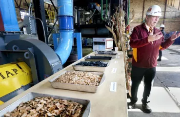 Don Fosnacht, NRRI associate director of the Renewable Energy Initiative, describes the process of converting wood (foreground) into compact briquettes that can be used in coal-fired power plants. Photo by Bob King, Duluth News Tribune