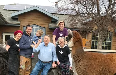 Ron and Kathy Gray, front right, along with (left to right) their daughter Miranda, son-in-law Scott, and grandchildren Murdock and Gwendolyn, pose with their rooftop solar energy system. Llamas from their family business join in the fun.