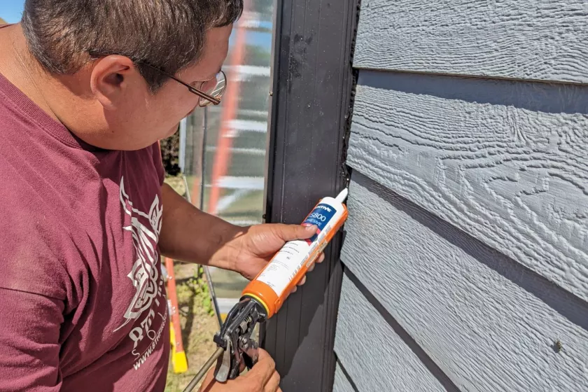 Man outdoors, using caulk gun on side of solar thermal panel