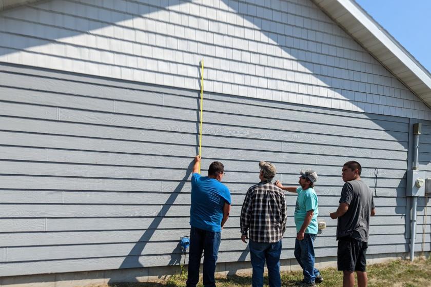 Outdoor side of home, four people measuring the side of the home with a measuring tape