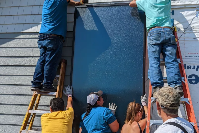 A group of men outdoors, hoisting a black panel onto the side of a home