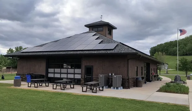 Large brown building in a park has a slanted roof with solar panels on two sides.