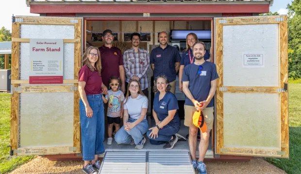 Nine people stand just inside a farmstand shed.