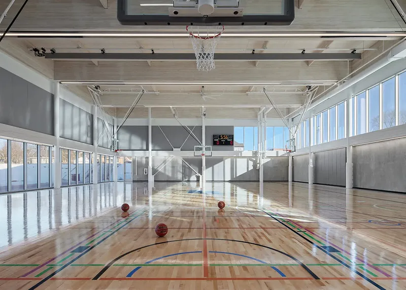 A few basketballs roll around on an indoor basketball court surrounded by windows.