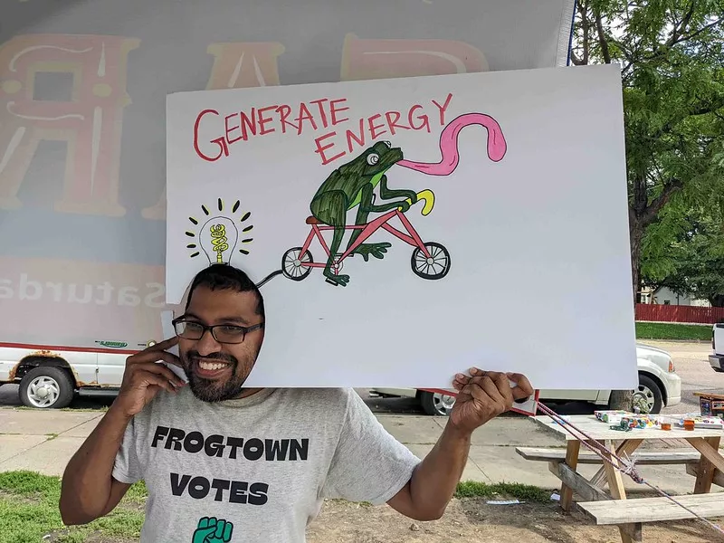 man holds poster called "generate energy" with a frog riding a bike